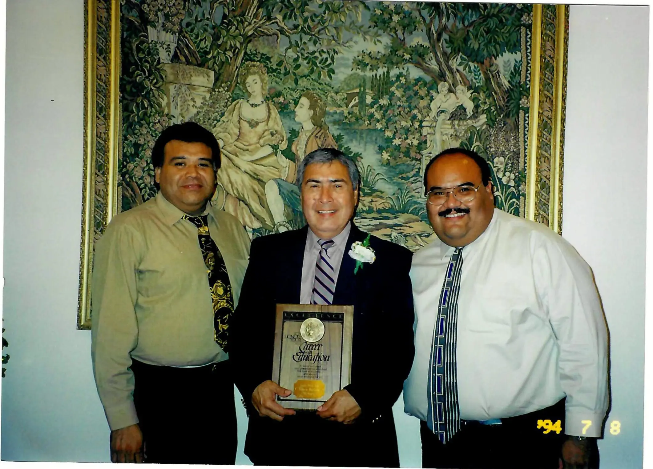 Three men posing with award and tapestry
