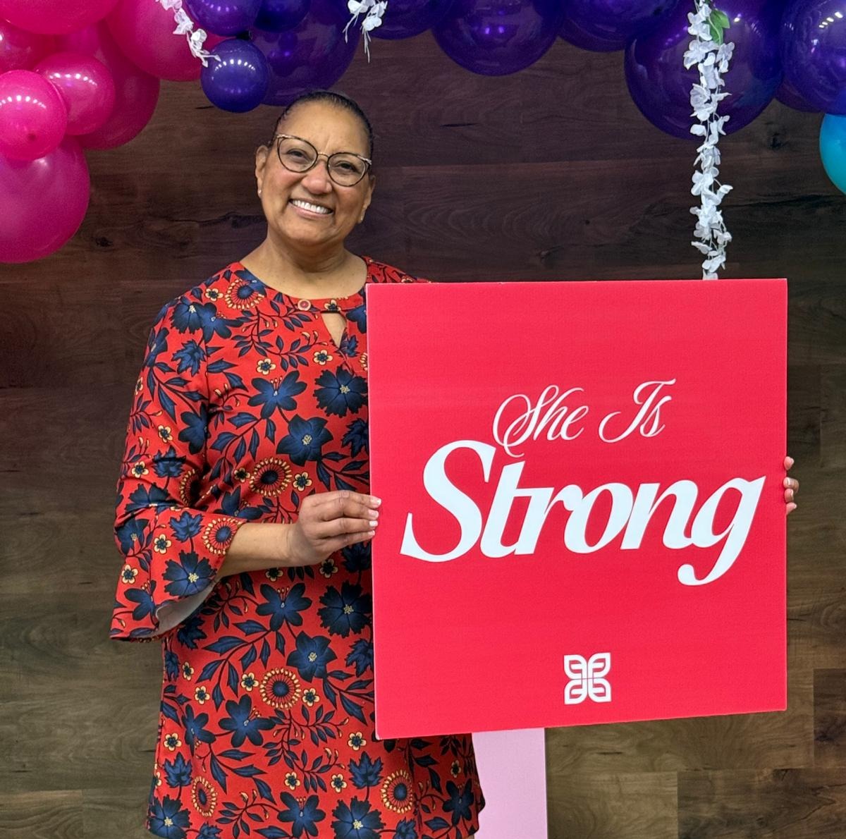 Smiling woman holding She Is Strong sign